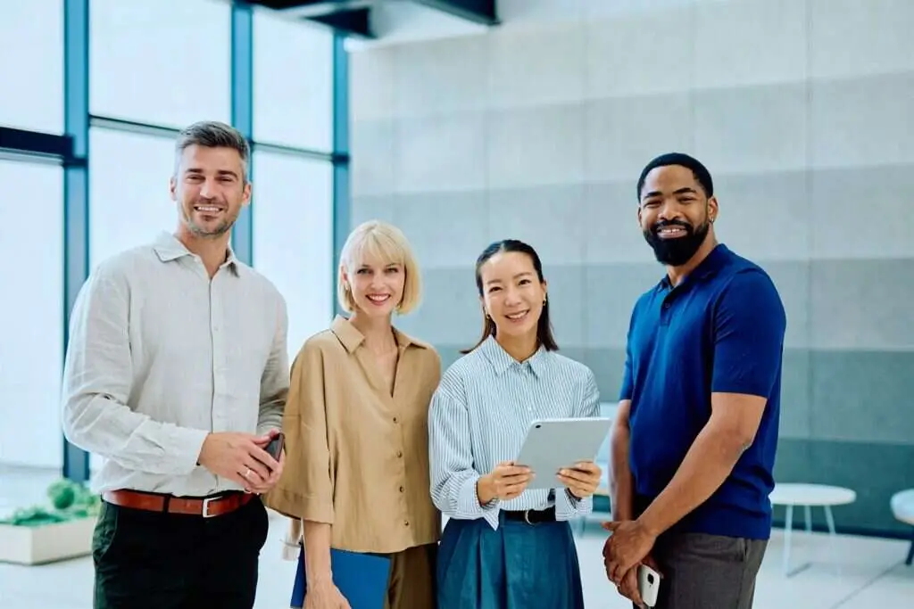 Four colleagues standing together in a bright modern office, one holding a tablet